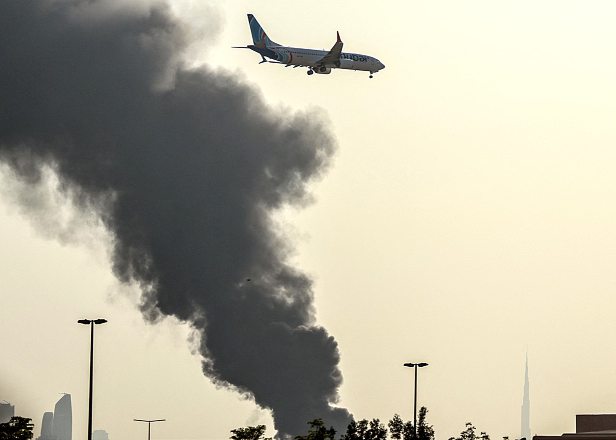 Le 16 mars 2026, un avion émirati s’apprête à atterrir, tandis que des colonnes de fumée s’élèvent près de l’aéroport de Dubaï. AFP