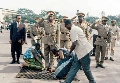 Cérémonie officielle de prise de pouvoir du colonel Joseph-Désiré Mobutu le 12 décembre 1965. Deux femmes, à genoux, lui essuient ses chaussures. RUE DES ARCHIVES/AGIP